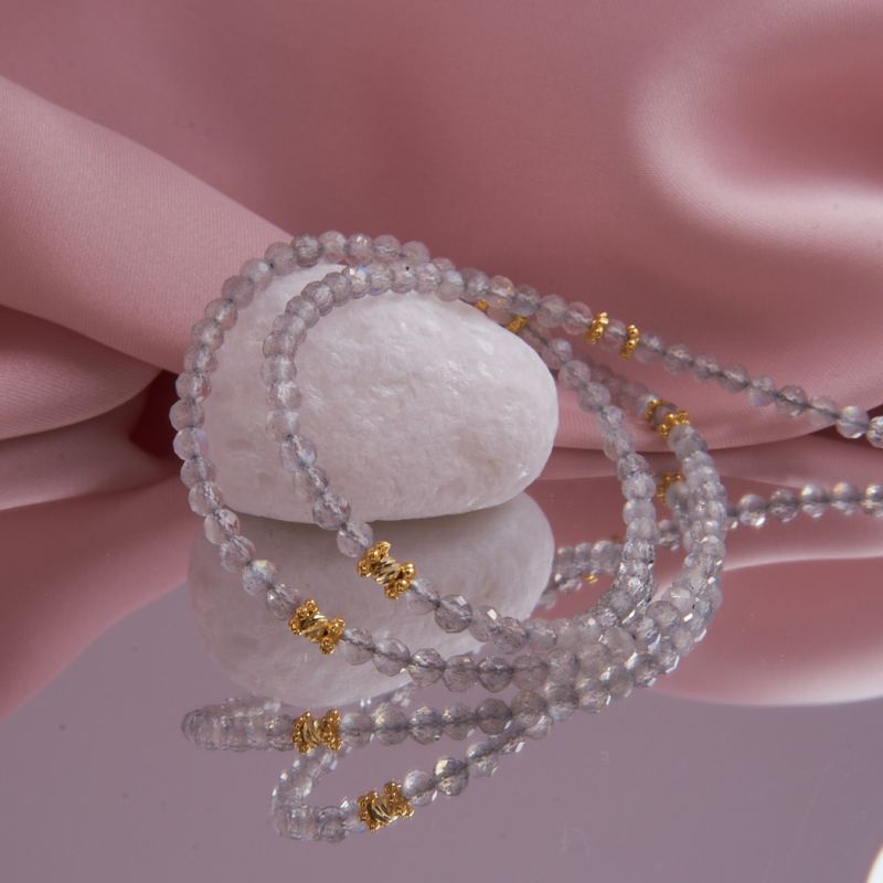 Nahaufnahme einer hochwertigen, facettierten Labradorit-Edelsteinkette in Grau mit blauem Schimmer und vergoldeten Silber-Zwischenelementen.